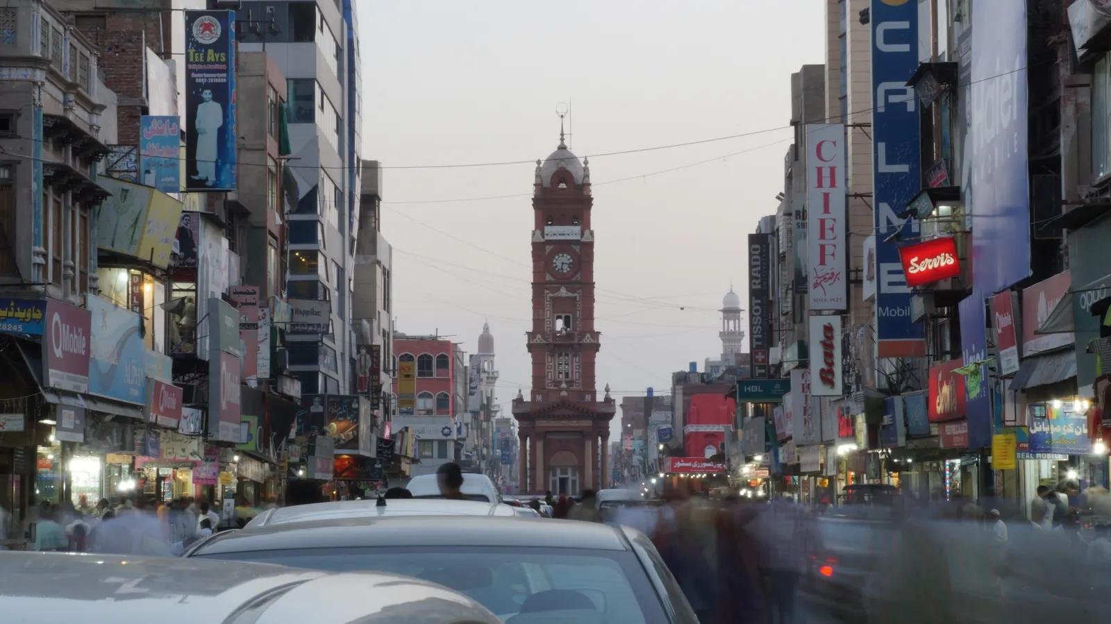 Faisalabad Clock Tower seen down a busy bazaar street lined with shop signs