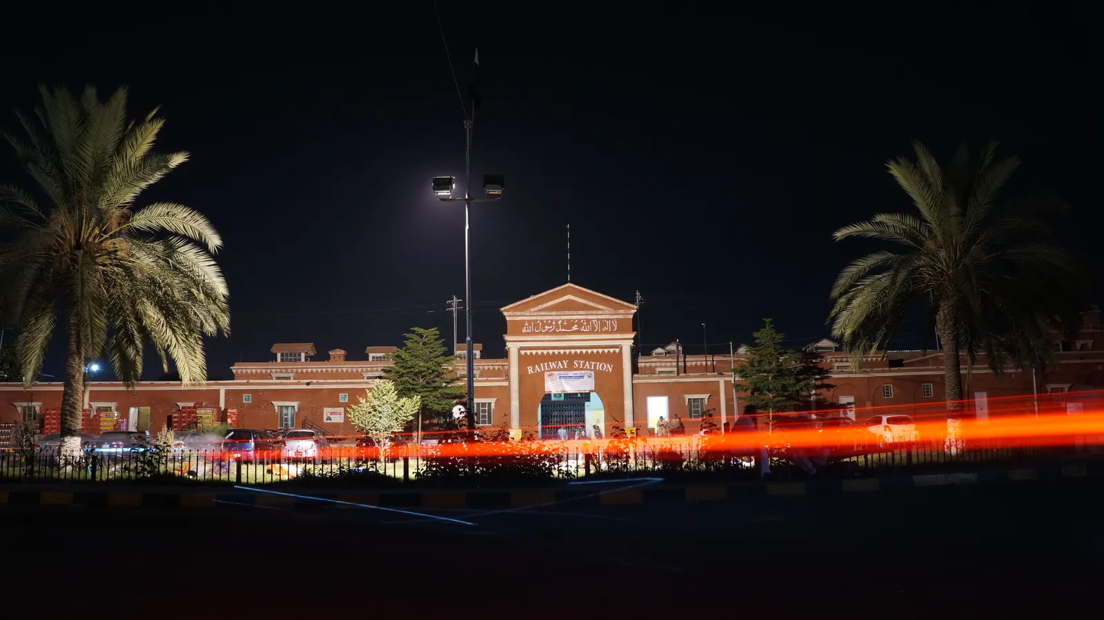 Faisalabad Railway Station at night with palm trees and light trails